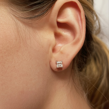 Close-up of an ear wearing a princess-cut diamond stud earring with blonde hair.